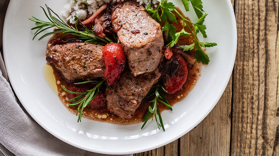 Pork tenderloin with plum sauce in a bowl on a wooden table