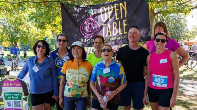 8 Members of the Open Table Ride for Food 2025 team with the black Open Table banner behind them