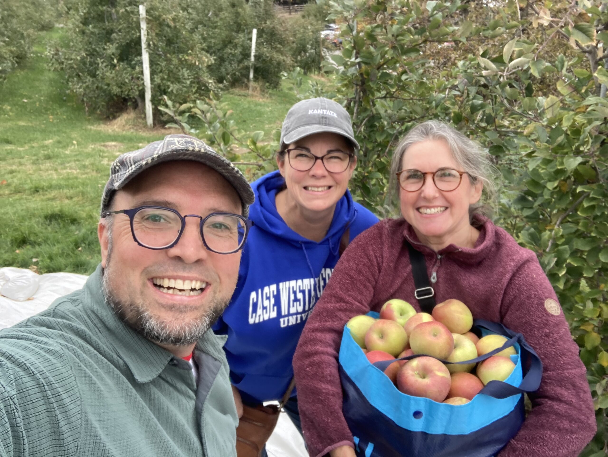 Three volunteers taking a selfie, one holding a bag of apples