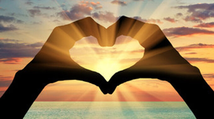 Hands forming a heart over a setting/rising sun