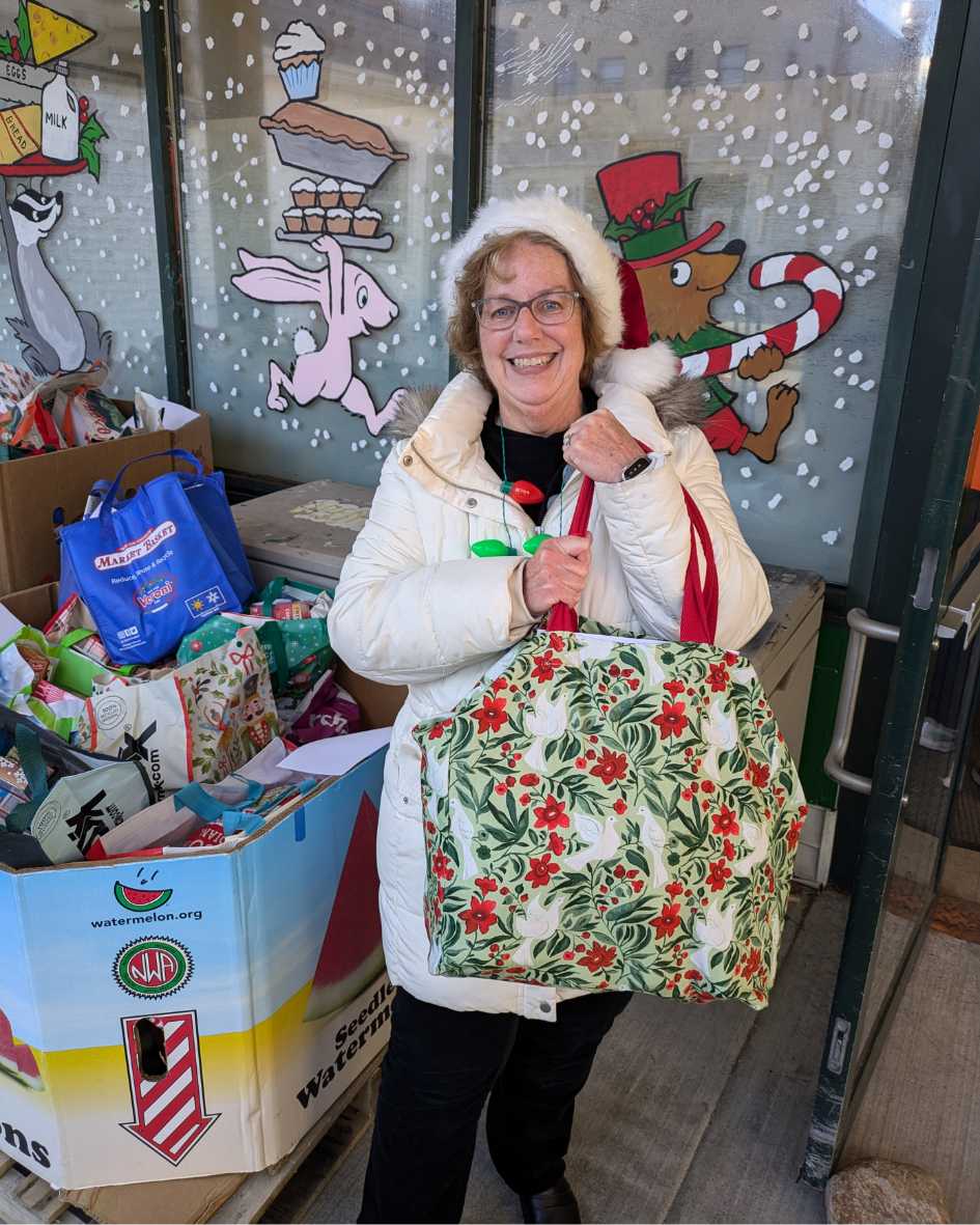 White woman in Santa Hat holding a large holiday bag